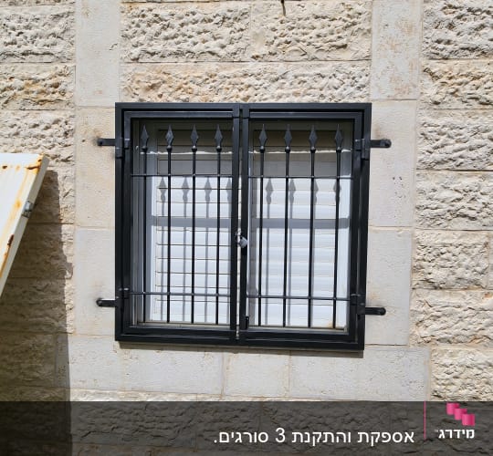 חלון עם סורגים שחורים על קיר אבן
